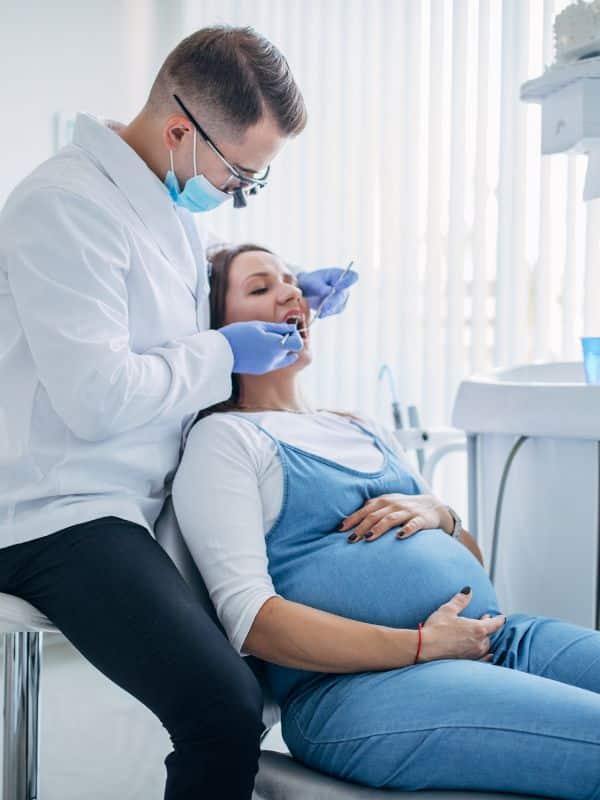 Pregnant woman sitting in dentist chair being worked on by dentist for check up