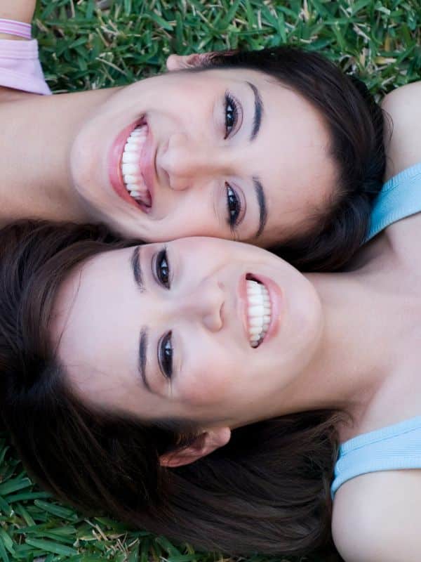 Two girls laying in grass cheek to cheek smiling