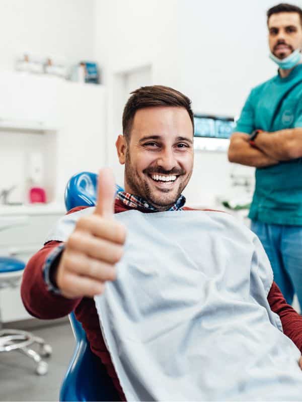 Man sitting in a dentist chair giving a thumbs up
